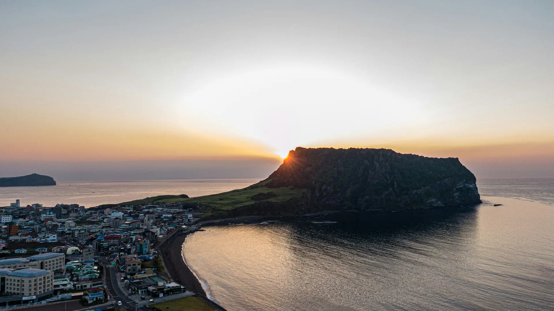 Sunrise over Seongsan Ilchulbong (Sunrise Peak) in Jeju Island, South Korea, viewed from above with the coastal village below — a must-visit for Muslim family travelers.