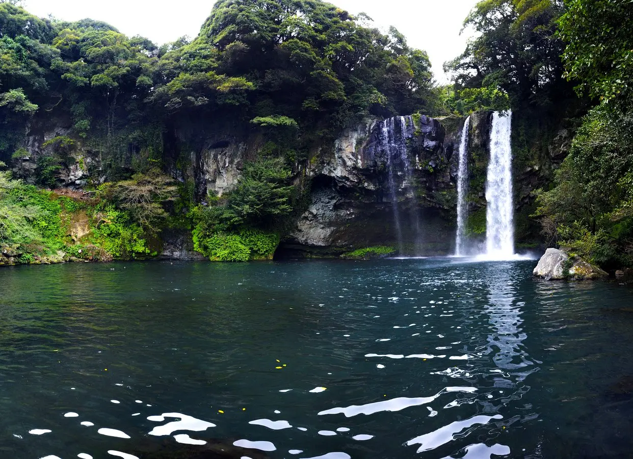 Cheonjiyeon Waterfall cascading into a clear pool surrounded by lush greenery in Jeju Island, South Korea — a serene nature spot ideal for family travel and peaceful prayer breaks.