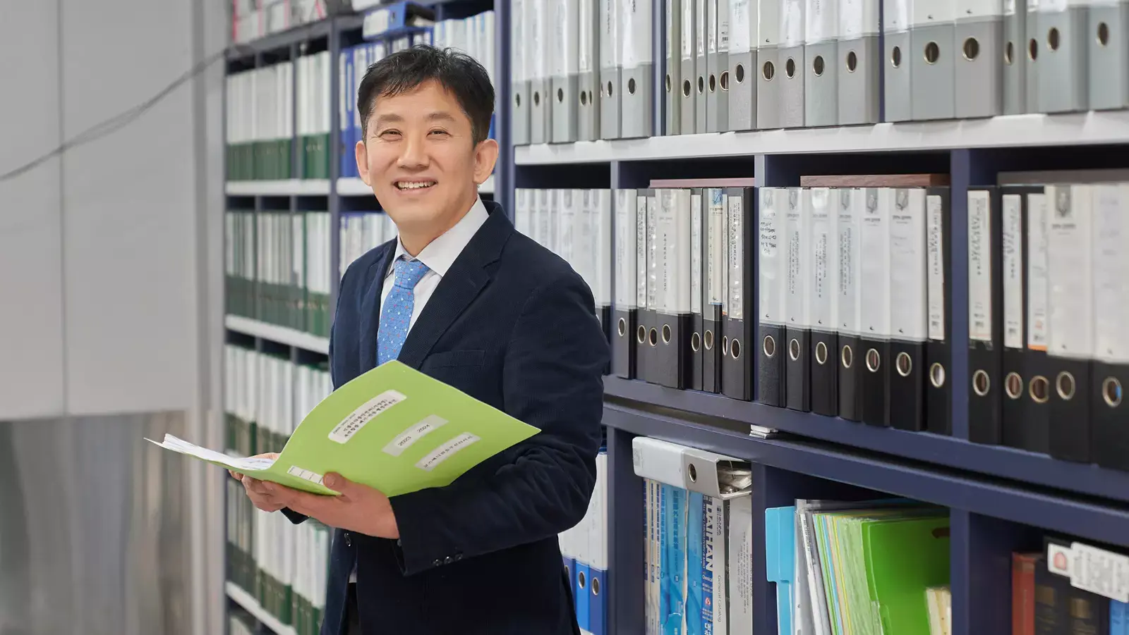 종이 파일을 들고 서고 앞에 서있는 남자