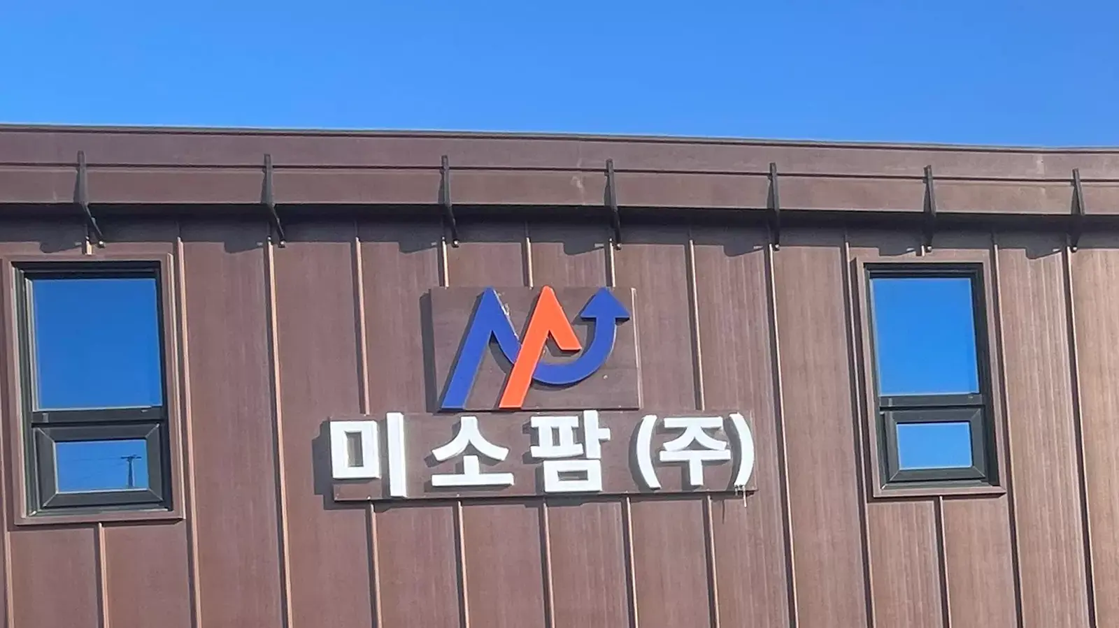 미소팜 주식회사 건물 외벽에 회사 로고와 이름이 크게 부착되어 있고, 청명한 하늘 아래 두 개의 창문이 위치한 모습