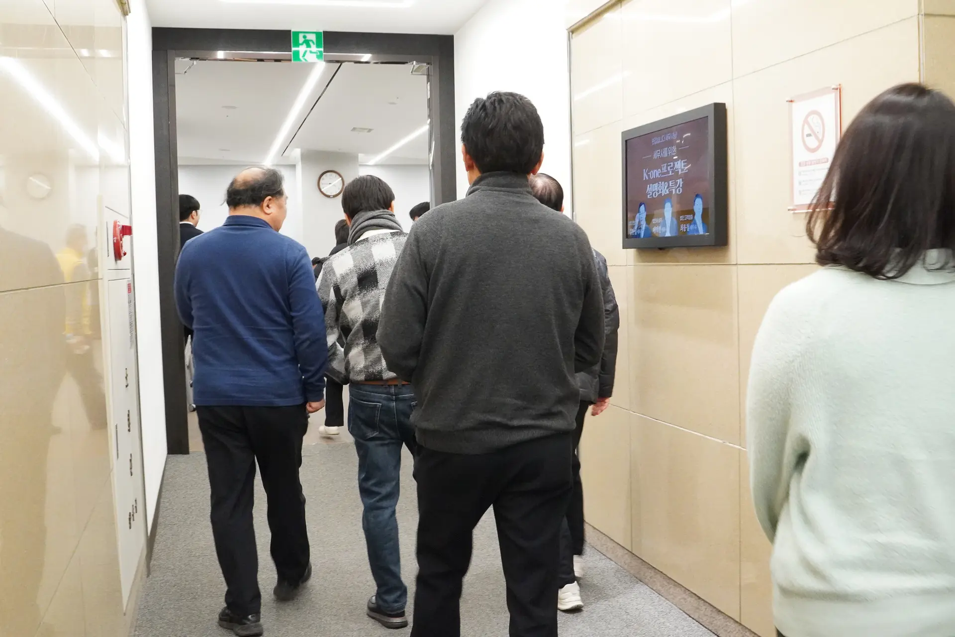 아이보리색 대리석 벽면과 회색 카펫이 깔린 복도, 그곳에서 설명회 참석을 위해 입장하고 있는 세무사들을 뒤편에서 촬영한 사진