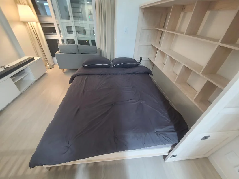 Fold-down double bed with charcoal bedding, open shelving, and a sofa by a large window (Listing ID : 16580)