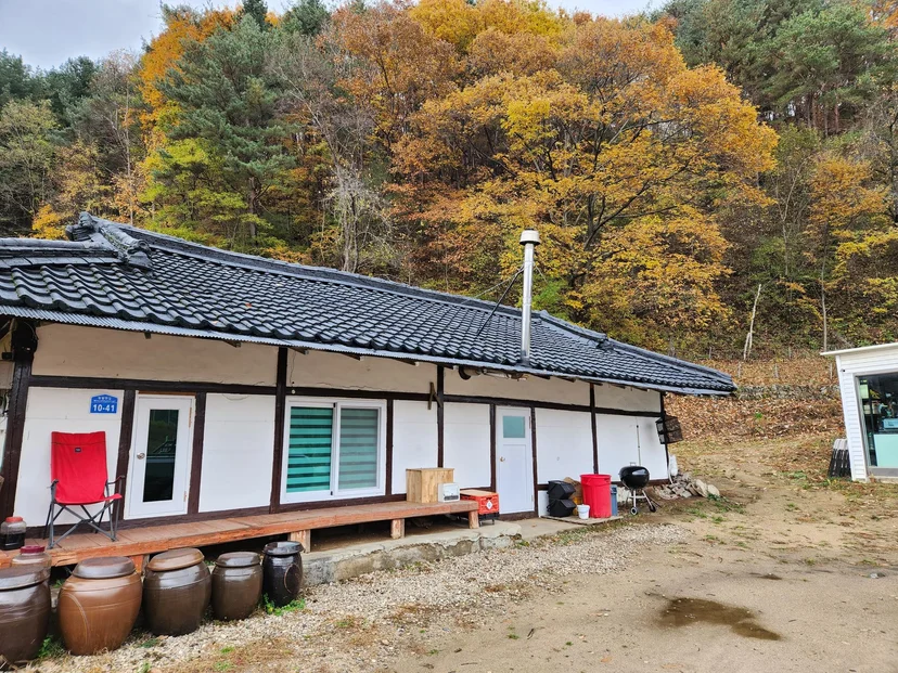 Hanok house with a black tile roof, wooden deck and autumn forest behind (Listing ID : 16916)