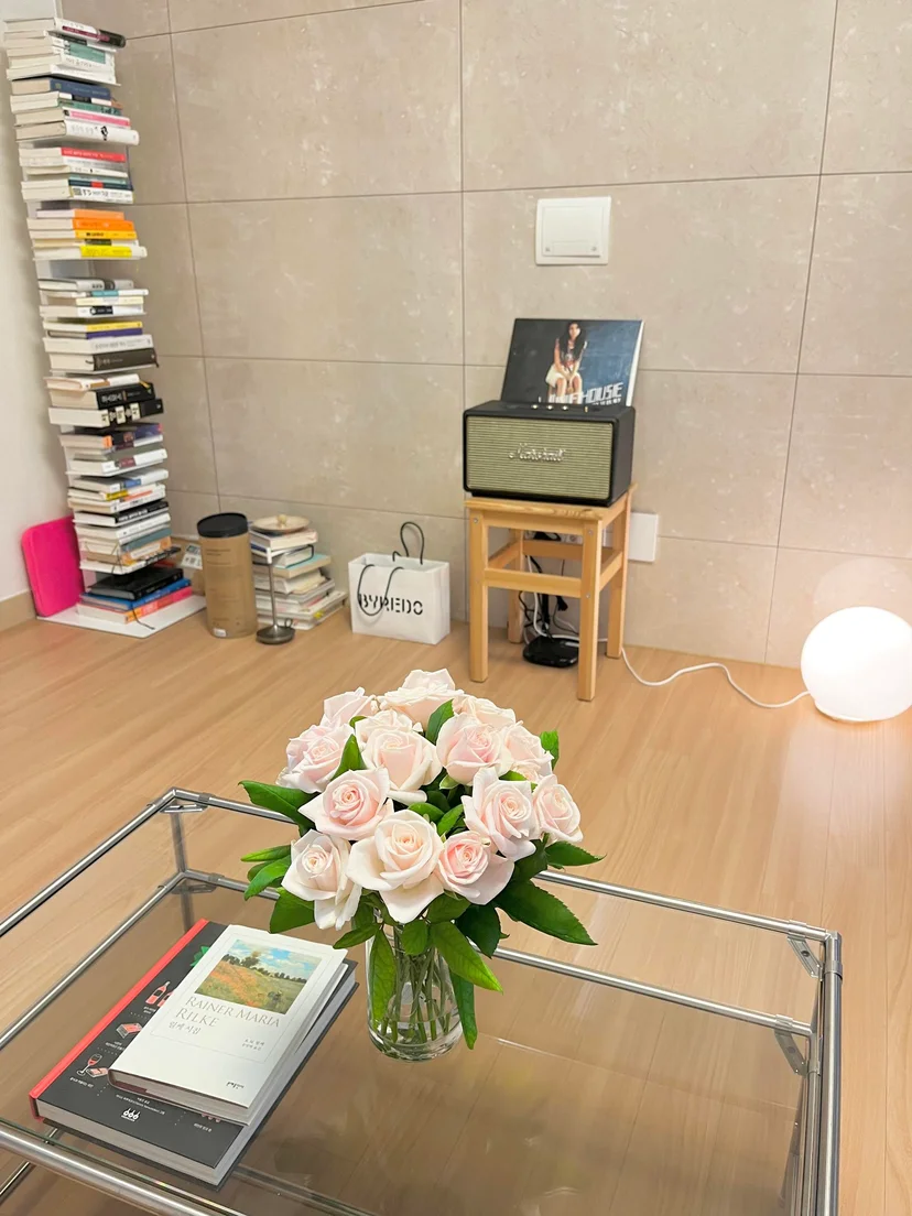 Room corner with a tall book stack, speaker on a wooden stool and roses on a glass table (Listing ID : 11764)