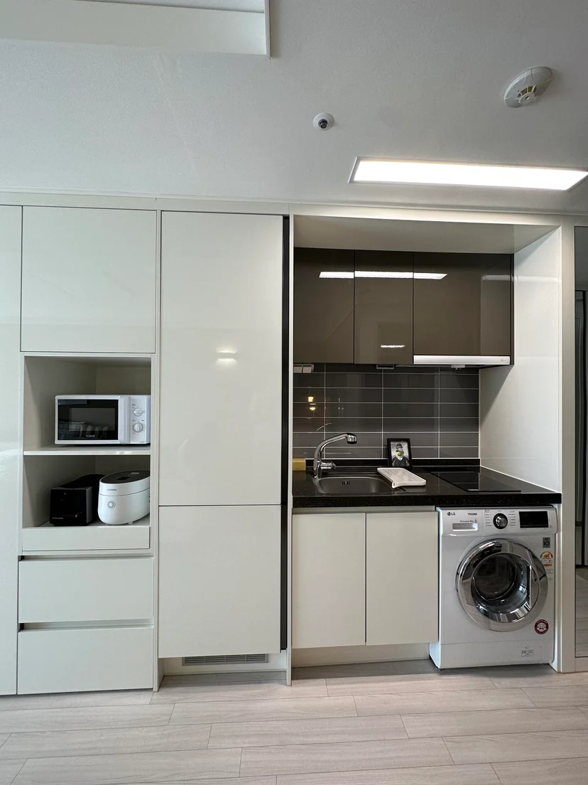 Compact kitchenette with white cabinets, a washing machine, sink, and microwave (Listing ID : 14405)