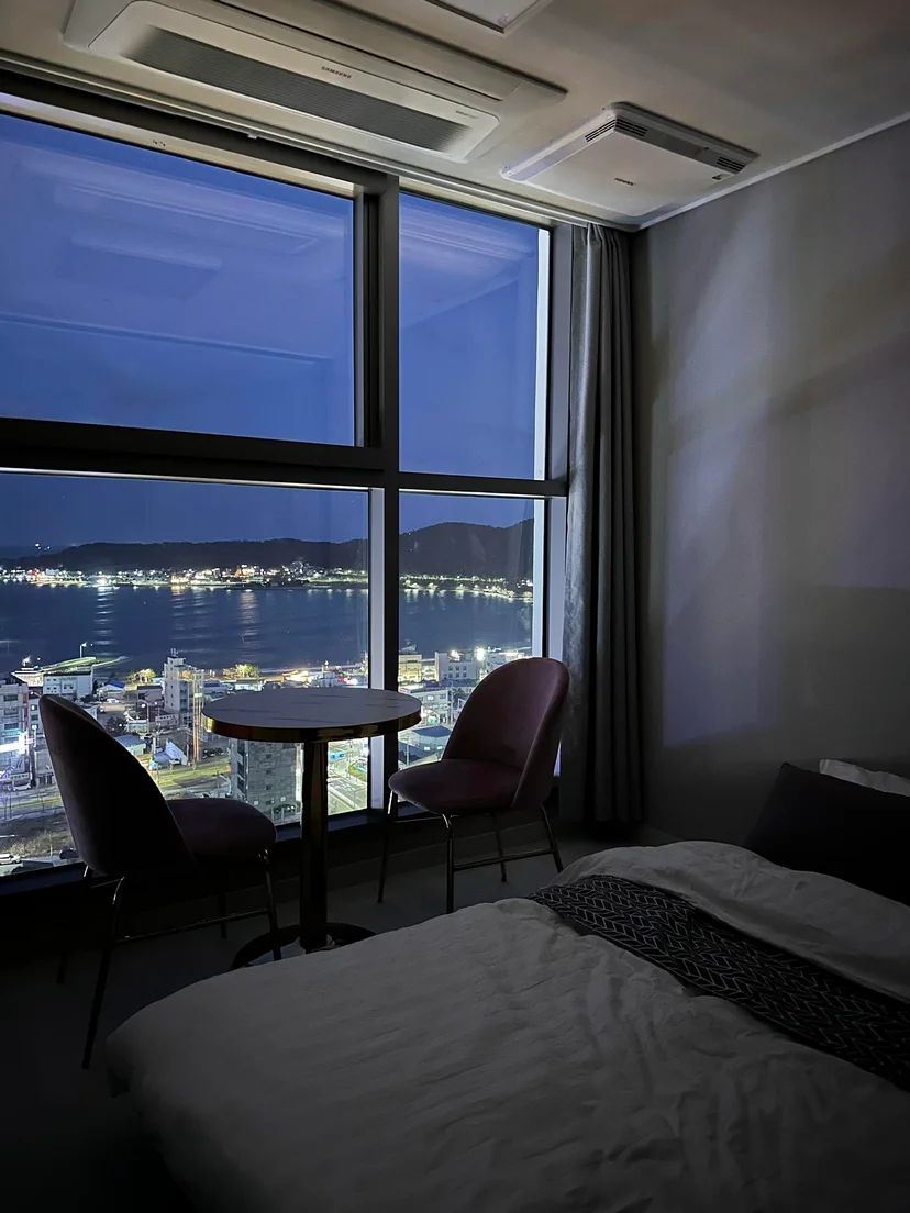 Studio at dusk with a bed, small table and a night view of the bay through large windows (Listing ID : 22344)