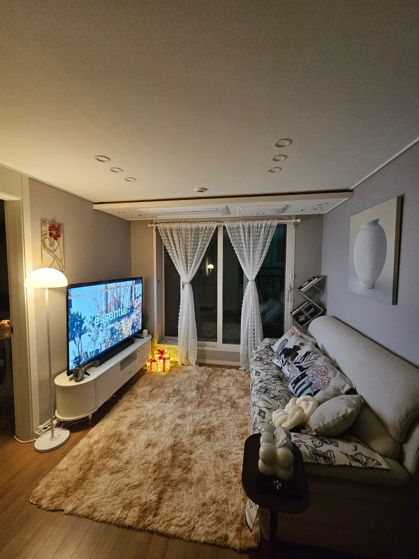 Cozy living room with beige sofa, large TV, sheer curtains, and floor lamp (Listing ID : 30308)