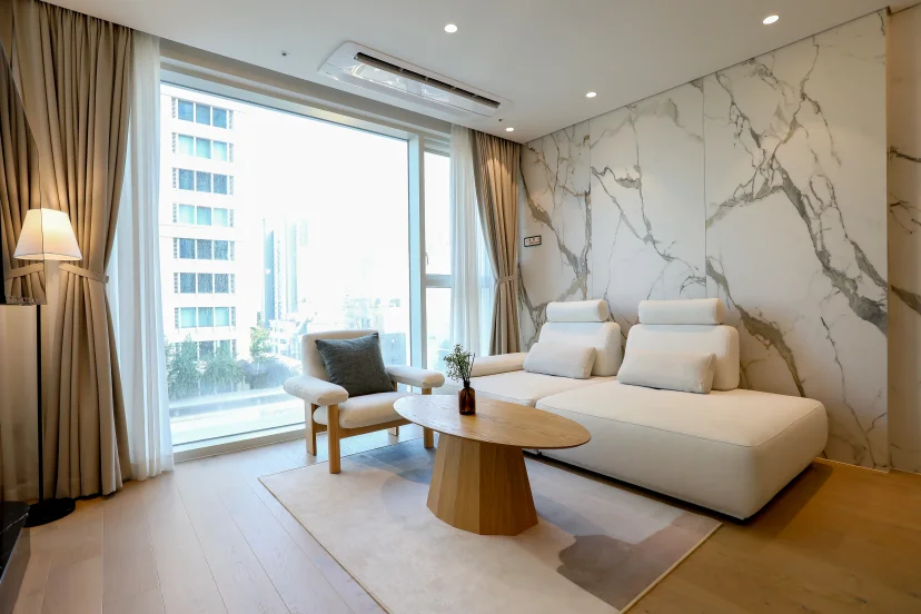 Living room with a cream sofa, oval coffee table and marble wall by a city-view window (Listing ID : 45208)