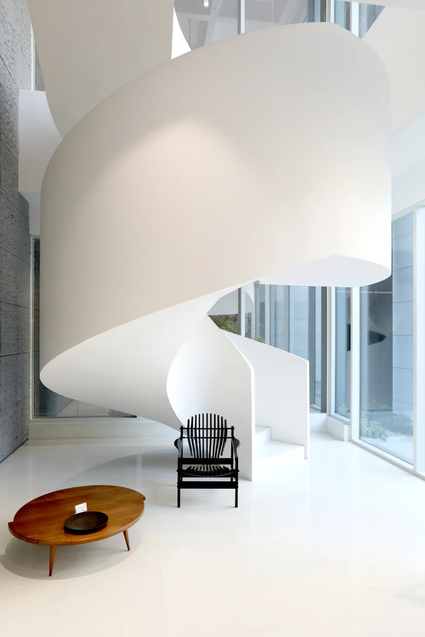 White spiral staircase in the building lobby with a black chair and oval wooden table (Listing ID : 45208)