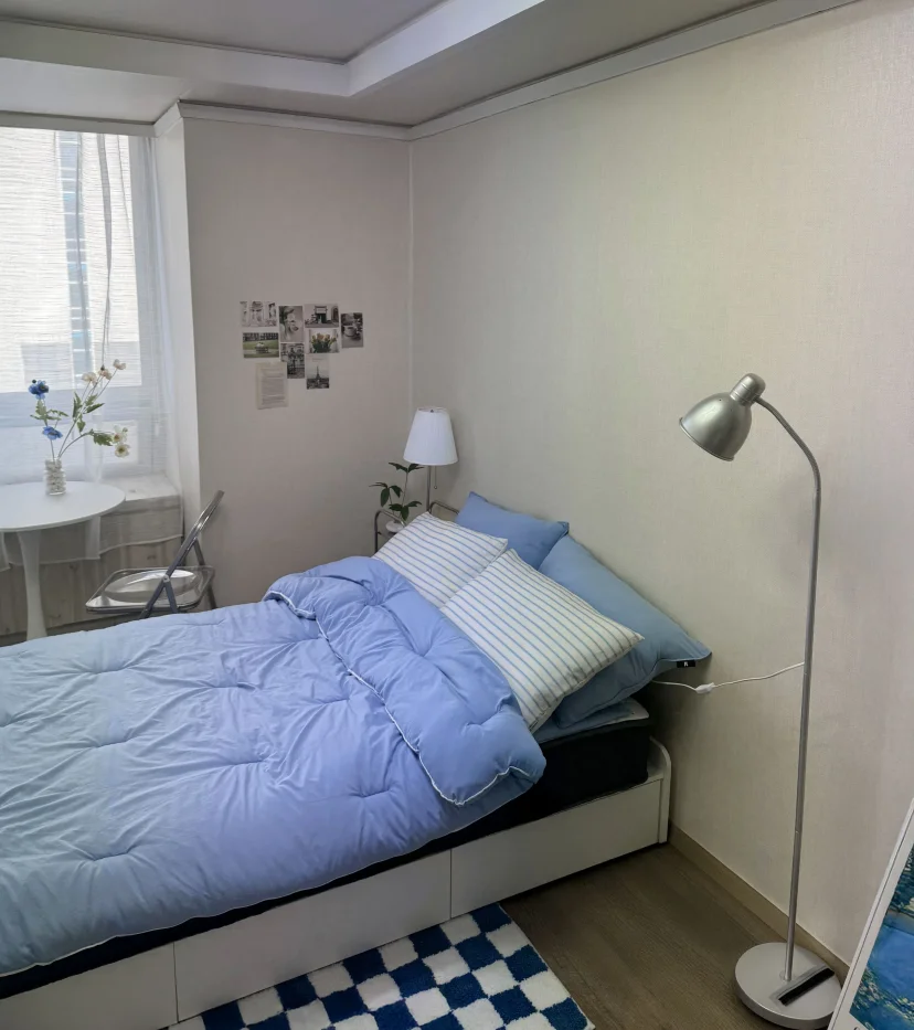 Studio bed with blue bedding next to a small window table (Listing ID : 45640)