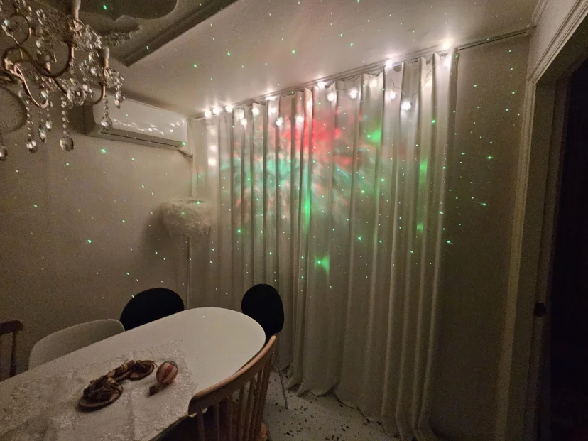 Dining area with curtains and chandelier lit by a colourful star-projector light (Listing ID : 46711)