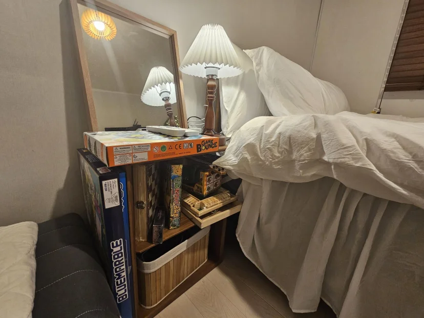 Bedside shelf with mirror, lamp and board games next to the bed (Listing ID : 46711)