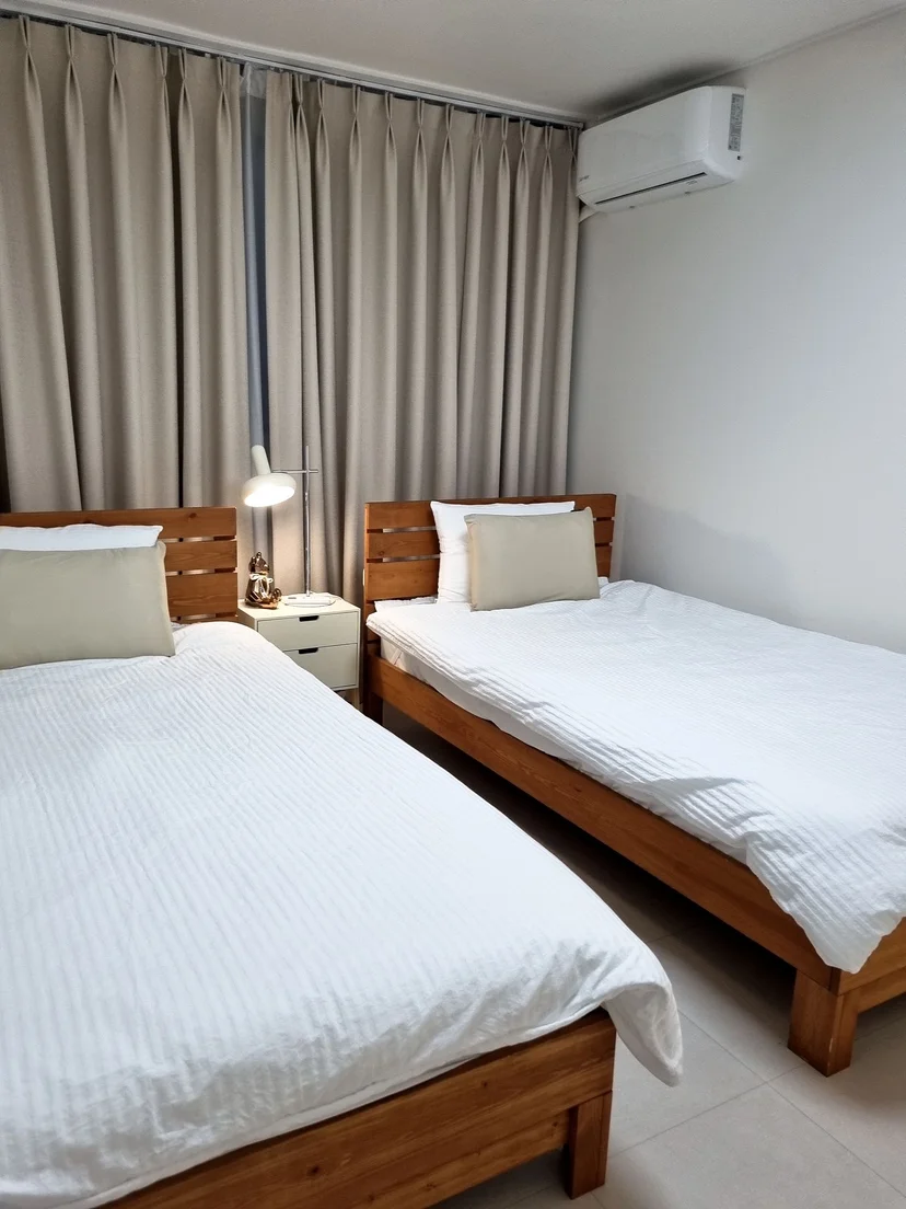 Bedroom with two single beds, wooden frames, and beige curtains (Listing ID : 38731)