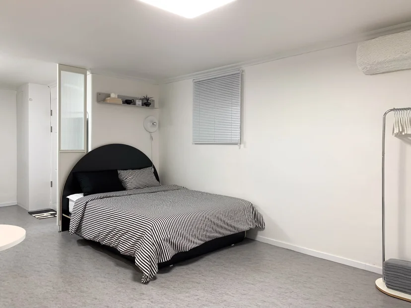 Wide view of the room with bed, blinds and clothing rack (Listing ID : 38554)