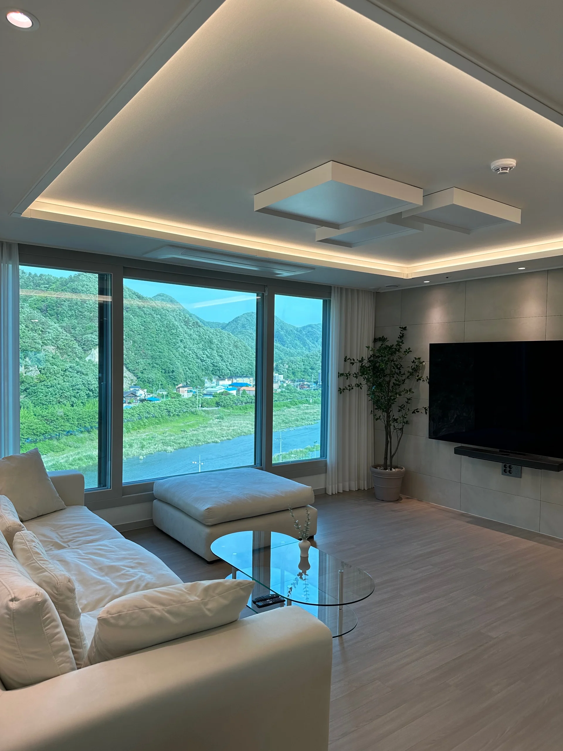 통창으로 산뷰가 보이는 거실, 흰 소파와 벽걸이 TV