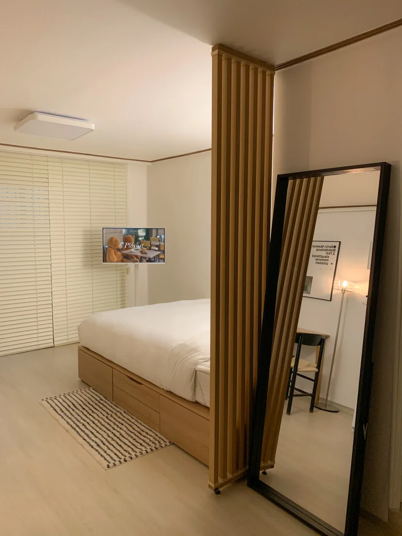 Bed behind a wooden slat partition with wall TV and a full-length mirror (Listing ID : 46336)
