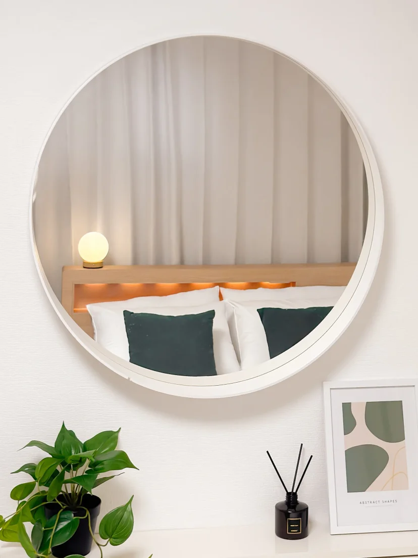 Round mirror reflecting the bed and a dresser with plants (Listing ID : 47877)