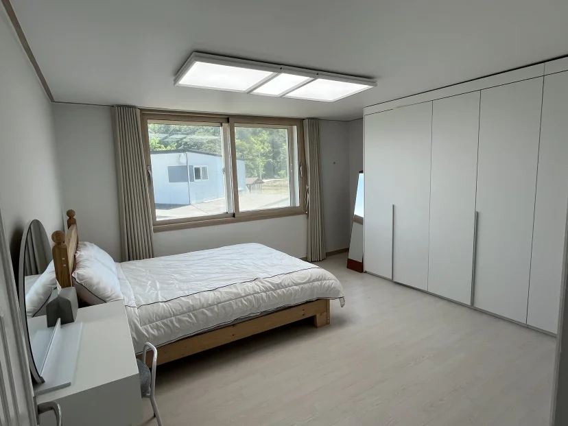 Bedroom with a wooden bed frame, built-in white wardrobe and a wide window (Listing ID : 51184)