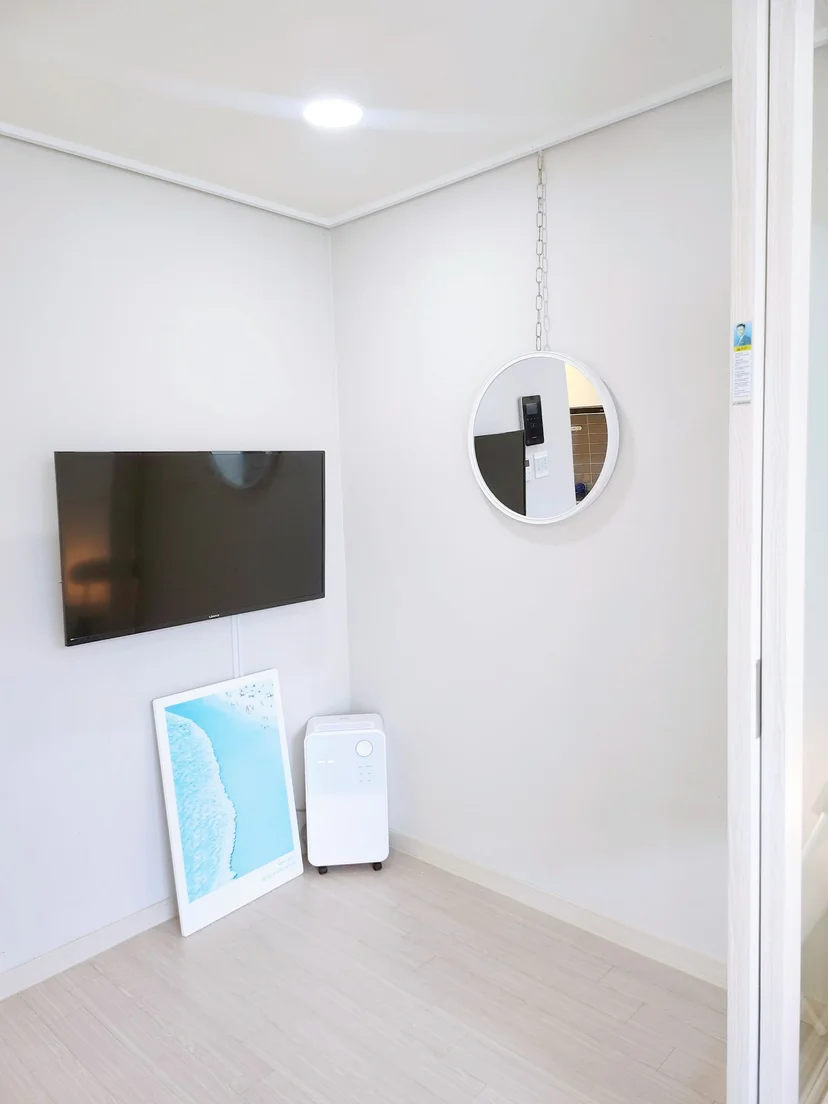 Room corner with a wall-mounted TV, round mirror and a portable dehumidifier (Listing ID : 27331)