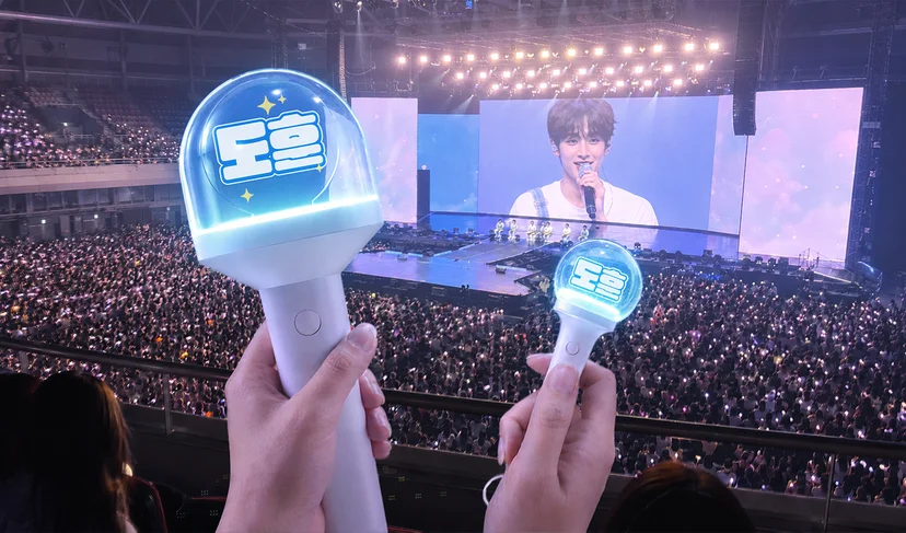 마플 원형 LED 응원봉 – 최애 이름을 넣은 투명 돔형 응원봉 2개를 파란색 조명이 켜진 콘서트장에서 무대를 향해 들고 있는 이미지
