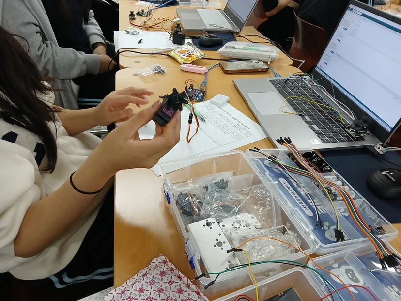 학생이 서보모터를 손에 들고 로봇 키트 부품을 조립하는 모습