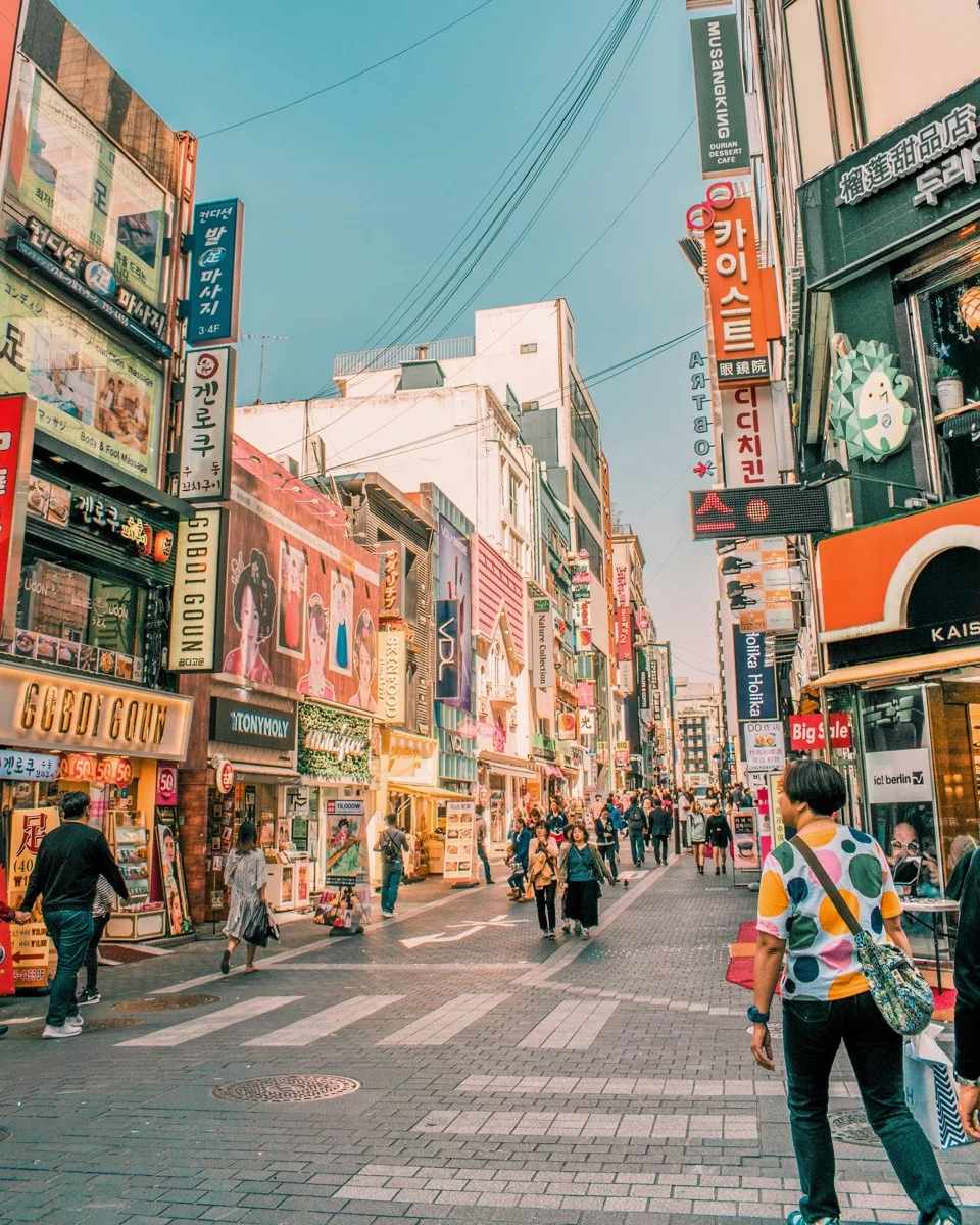Busy Myeongdong shopping street in Seoul with crowds of people walking between colorful storefronts and signs