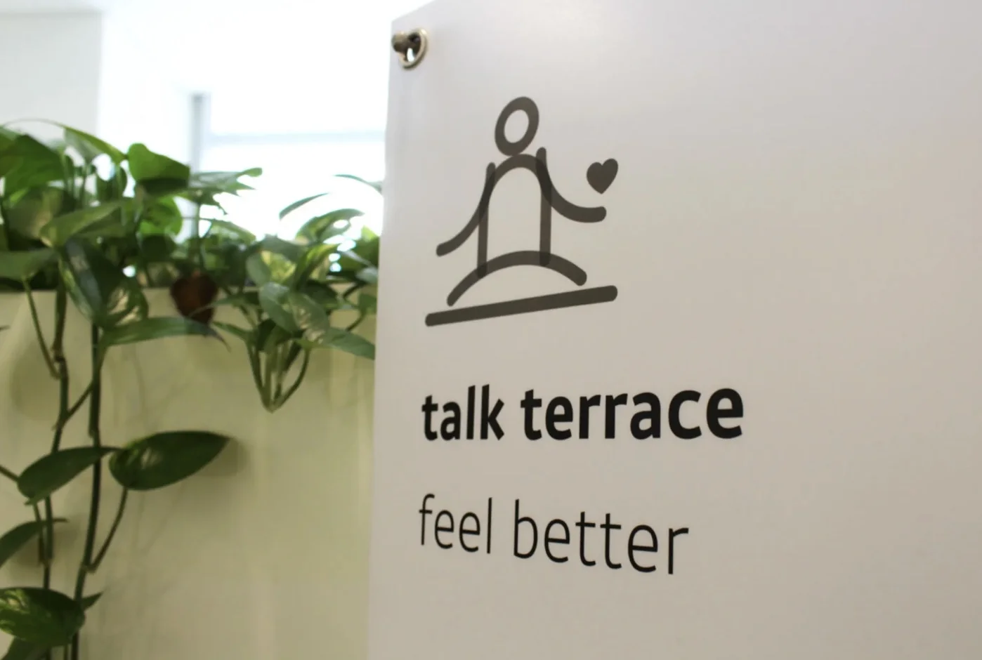 카카오의 직원 웰니스 공간인 '톡 테라스' 앞에 설치된 배너. 사람 형태의 플래티콘과 작은 하트 이모지가 그려져 있고, 아래에 굵은 글씨의 영어로 'talk terrace', 'feel better'이라 쓰여 있다. 