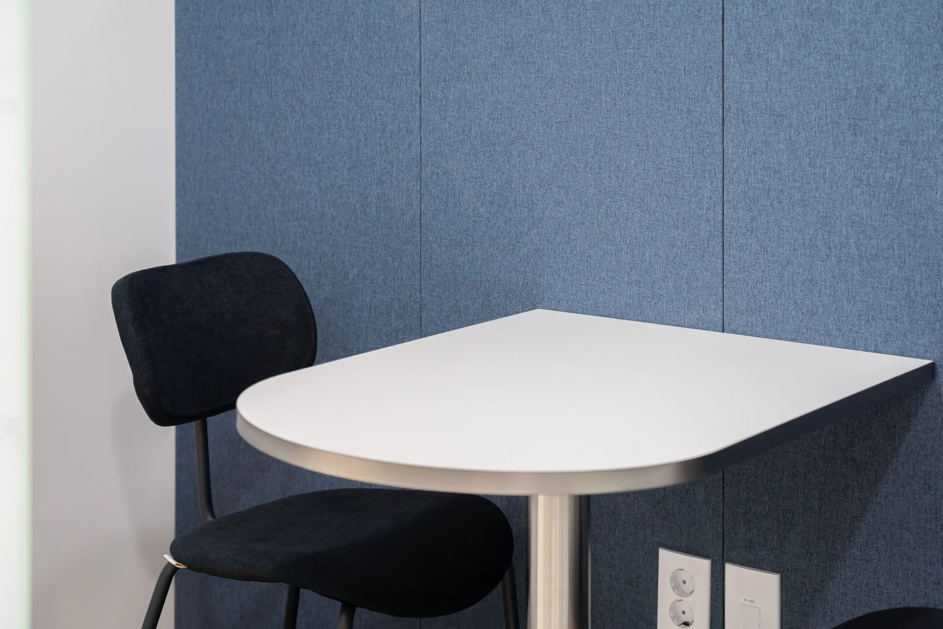 모던한 오피스 인테리어의 소규모 미팅 공간으로, 파란색 흡음 패널 벽과 흰색 반원형 테이블, 검은색 의자가 조화롭게 배치되어 있습니다. 미니멀한 디자인의 스타트업 사무실 인테리어로 프라이버시와 집중을 위한 공간입니다.
