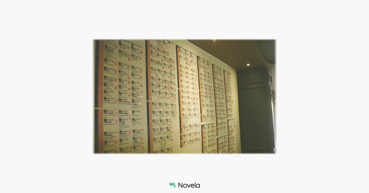 영화관 벽면을 따라 빼곡히 붙어 있는 수많은 영화 상영 일정표를 촬영한 사진. 조명이 은은하게 비치는 공간 안에 제각기 다른 제목을 가진 영화들이 정렬되어 있으며, 그 자체로 수많은 이야기의 가능성을 암시한다. 이 사진은 전주국제영화제 현장에서 촬영된 것으로, 다양한 서사들이 한 공간에 모여 있는 풍경을 보여준다. 하단 중앙에는 Novela 로고가 배치되어 있고, 이 이미지는 “우리를 둘러싼 세상이라는 이야기”라는 글과 함께 사용된다. 글은 신문, 역사, 신화, 예술 등 외부의 세계에서 영감을 얻을 수 있는 창작의 출발점을 제시하며, 영화제 같은 이야기의 장을 찾아가 보는 경험의 중요성을 강조한다.