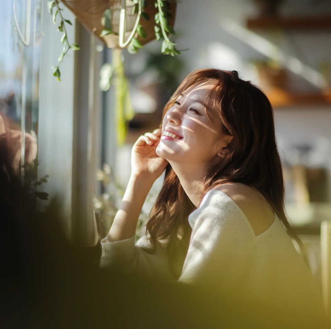 창가에 앉아 햇살을 받으며 미소 짓는 한국 여성의 감성 브이로그 썸네일 – 따뜻한 노란빛 자연광과 흐릿한 실내 배경이 어우러진 편안한 분위기의 장면