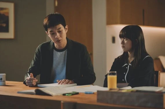 영화 《기생충》의 한 장면으로, 기우(최우식)가 부잣집 딸 다혜에게 과외를 하는 모습. 식탁에 나란히 앉아 있는 두 사람 사이에는 교재, 노트, 펜, 형광펜, 주스잔 등이 놓여 있으며, 조용한 밤의 긴장된 분위기 속에서 서로를 응시하거나 외면한다. 1인칭 시점과 주인공 내면에 몰입하는 이야기 구조를 설명하는 문단과 함께 배치된 이미지로, 관객이 기우의 시선에 감정이입하는 방식을 강조하는 용도로 사용되었다.