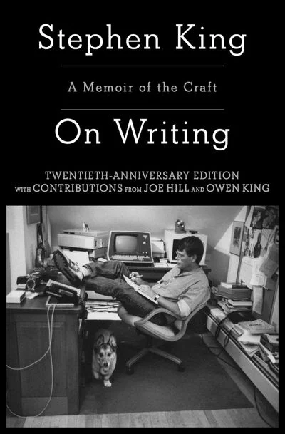 스티븐 킹 저서 『On Writing: A Memoir of the Craft』 20주년 기념판 표지 이미지. 표지 상단에는 “Stephen King”이라는 저자명이 흰색 세리프체로 강조되어 있고, 그 아래 “A Memoir of the Craft”, “On Writing”이라는 제목이 정갈하게 배열되어 있다. 하단에는 “Twentieth-Anniversary Edition with contributions from Joe Hill and Owen King”이라는 설명 문구가 추가되어 있어, 아들인 조 힐과 오언 킹의 기고가 포함된 특별판임을 알 수 있다. 표지 하단 흑백 사진에는 젊은 시절의 스티븐 킹이 책상 앞에 다리를 꼬고 앉아 타자기를 두드리는 모습이 담겨 있다. 주변엔 책과 서류가 가득하고, 책상 아래에는 반려견이 앉아 있다. 작가의 실제 집필 공간이자 창작의 순간을 포착한 이미지로 구성되어 있다.
