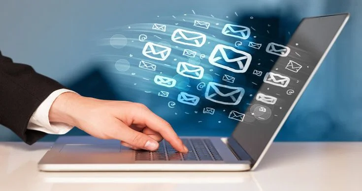 Hand typing on a laptop with email icons flying out, representing email marketing or mass email communication