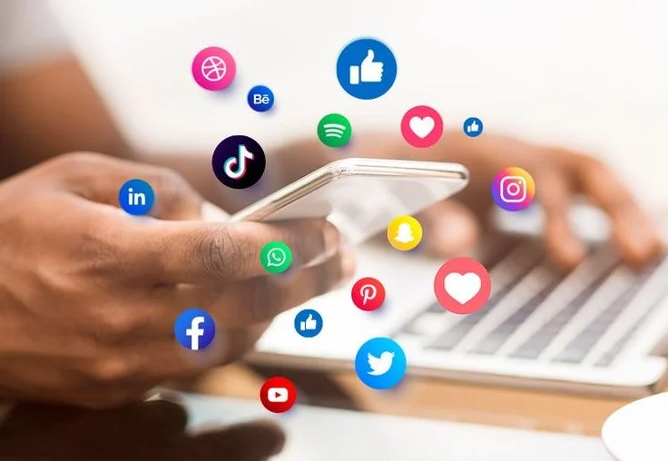 Person using smartphone and laptop surrounded by floating social media icons including Facebook, Twitter, Instagram, TikTok, and LinkedIn, symbolizing digital marketing and social media engagement