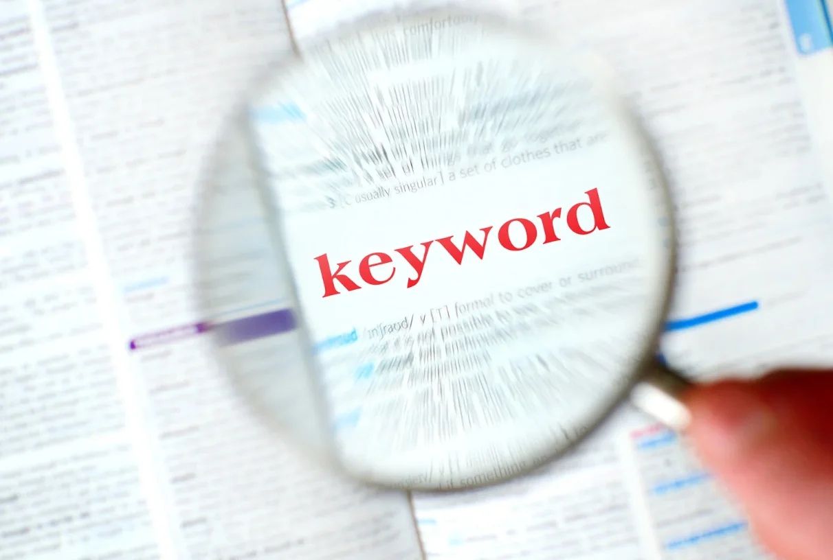 Magnifying glass highlighting the word "keyword" in a dictionary, symbolizing the importance of keyword research in SEO and content marketing
