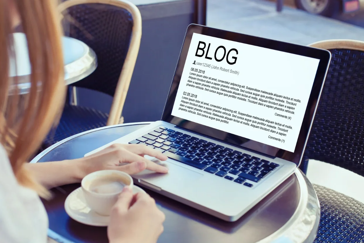 Person reading a blog post on a laptop while drinking coffee at an outdoor café table