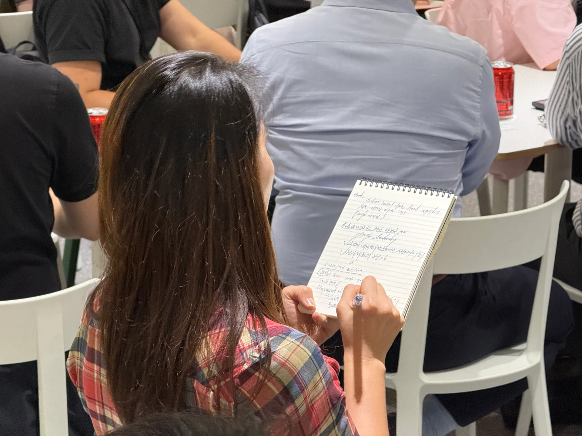 업피플 리더십 세미나의 참석자 중 한 명이 파란색 펜과 스프링 노트를 들고 메모에 열중하고 있다.