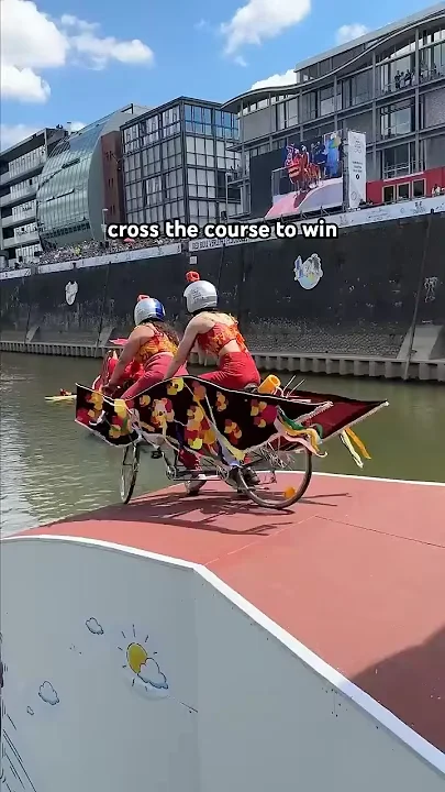 레드불 유튜브 콘텐츠로 두 사람이 우스꽝스러운 장식을 한 자전거를 타고 물 속을 향해 달려가고 있다.