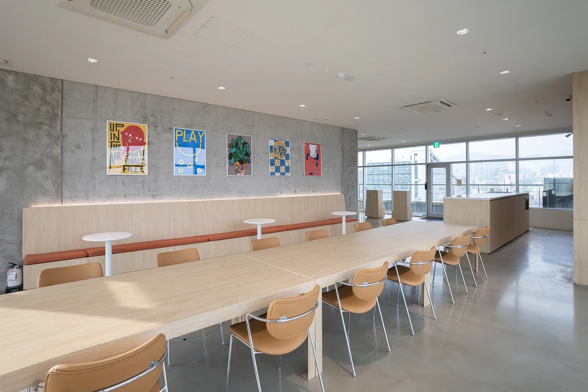 맹그로브 신설의 20층에 위치한 시티라운지의 전경을 비스듬히 바라본 모습. 가로로 긴 업무용 테이블에 베이지 색 가죽 의자들이 나란히 서로 마주보며 놓여있고 오른 쪽 통 유리창을 통해서는 서울의 전경이 한 눈에 보이고 있다.