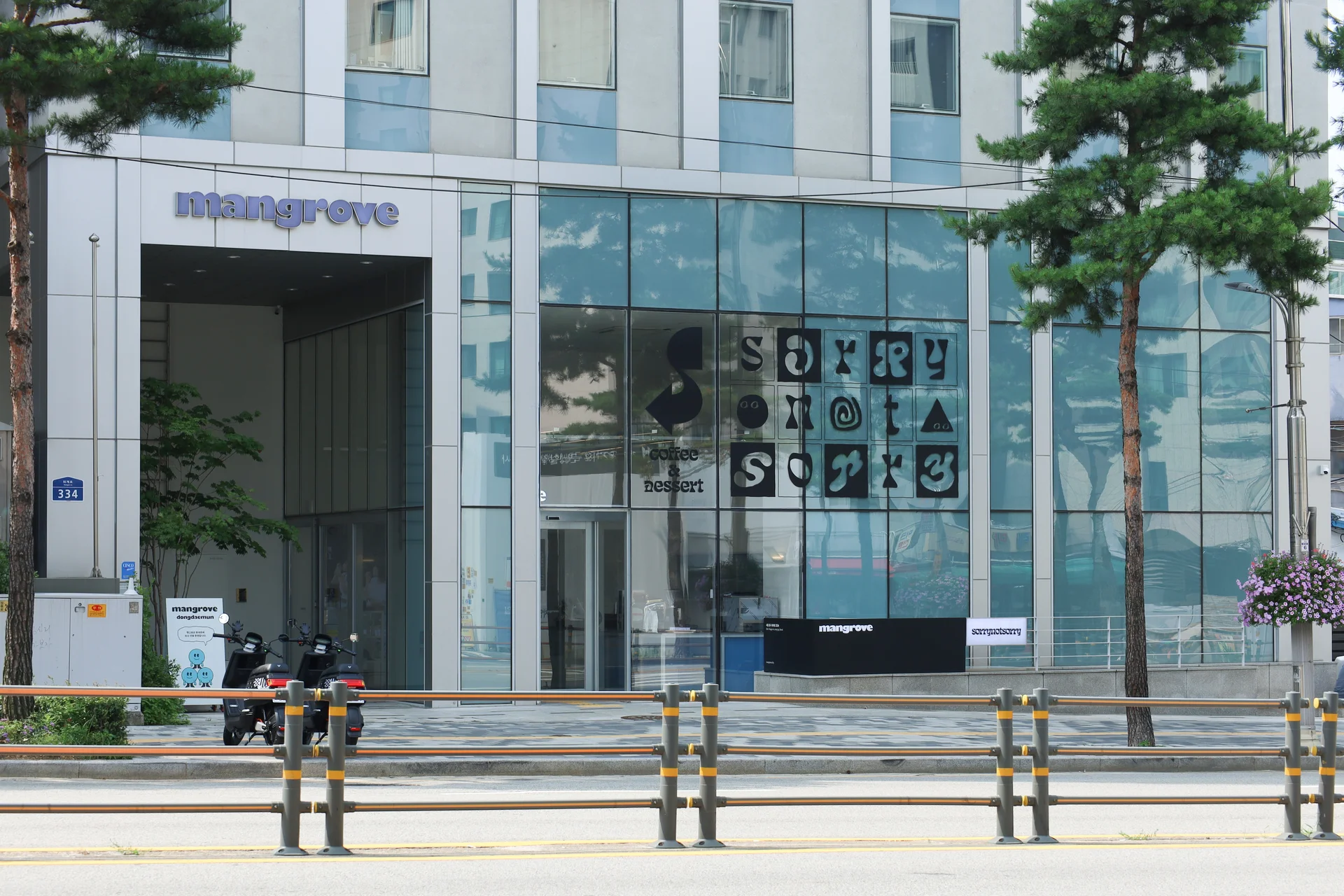 맹그로브 동대문 건물 1층 외부 전경. 전면 유리 파사드와 ‘mangrove’ 간판이 보이며, 내부에는 레터링 아트워크와 리셉션 데스크가 보인다. 도로와 가로수, 출입구 주변의 작은 조경이 함께 어우러져 있다.