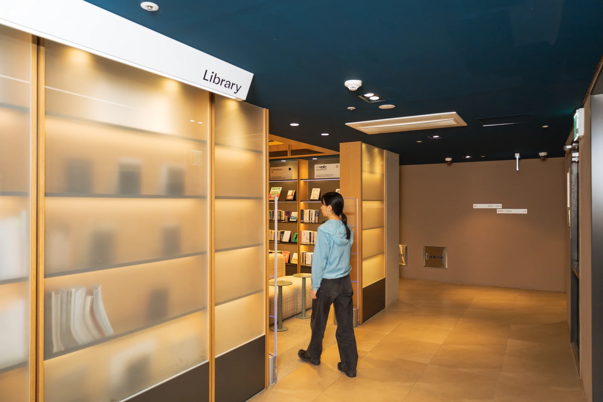 서울 맹그로브 신촌 라이브러리 입구 전경. 유리 파티션과 조명이 따뜻한 분위기를 조성하며, 책장이 보이는 도서관 공간으로 입주민과 장기 숙박 이용객이 독서와 학습에 활용할 수 있는 공용 공간. 맹그로브 신촌 코리빙 주거 공간의 대표적인 커뮤니티 시설 중 하나.