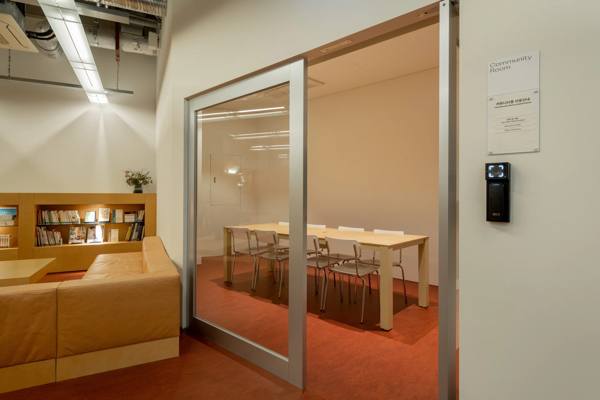 서울 맹그로브 동대문 B1 라이브러리와 커뮤니티룸 공간. 유리 파티션으로 구분된 회의실에는 테이블과 의자가 마련되어 스터디 모임, 회의, 워크숍 등 다양한 커뮤니티 활동이 가능하다. 외부에는 서재형 책장과 소파가 배치되어 입주민과 장기 숙박 이용객이 독서와 휴식을 즐길 수 있는 코리빙 공용 공간.