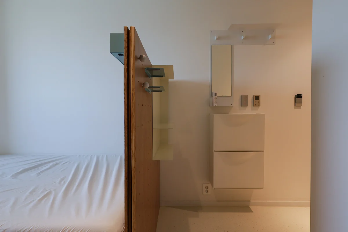 서울 맹그로브 신설 싱글룸 개인 공간. 침대 옆에 분리된 벽면에는 거울과 수납장이 설치되어 있고, 미니멀한 화이트 인테리어가 특징이다. 장기 숙박과 1인 생활에 적합한 코리빙 하우스 객실로, 깔끔한 수납과 개인 위생 관리가 가능한 효율적인 공간.