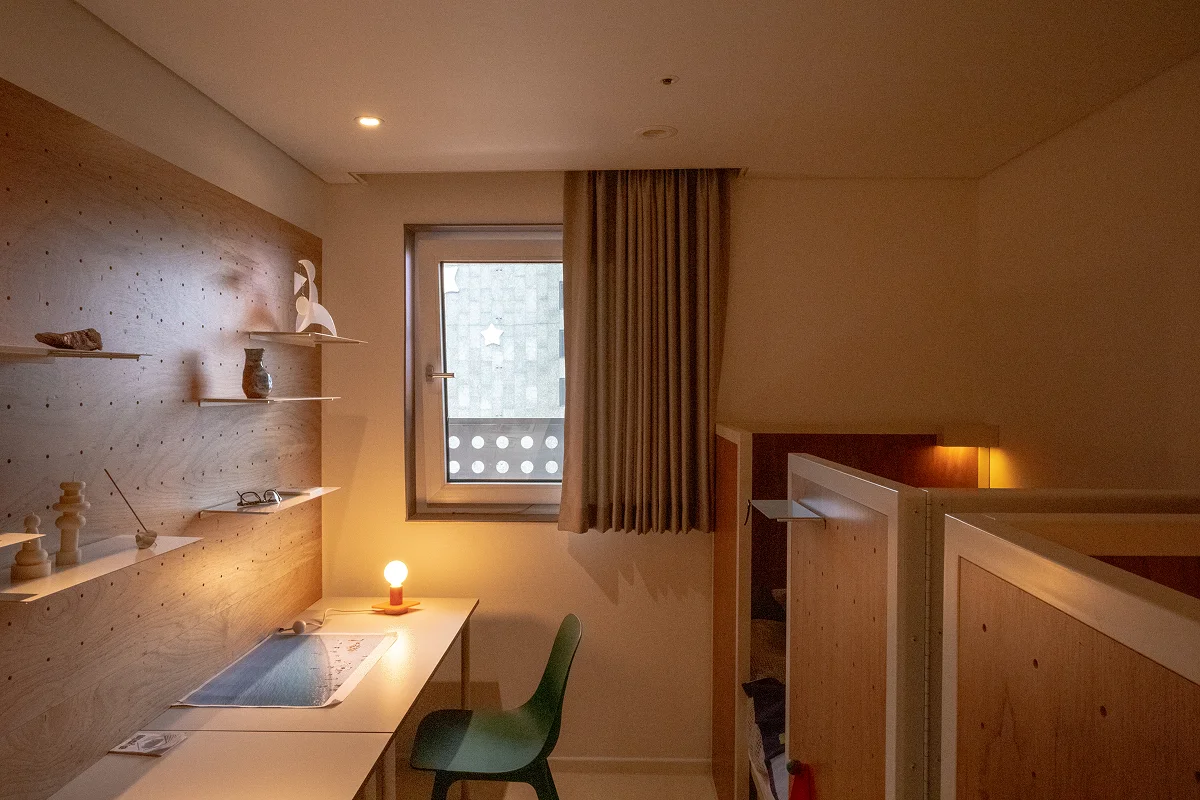 맹그로브 신설 장기 숙박 Twin Deluxe 룸 전경 – 우드톤 인테리어의 아늑한 객실로, 창가 책상과 의자, 조명이 갖춰져 장기 체류 고객이 공부와 업무, 휴식을 모두 누릴 수 있는 코리빙 공간.