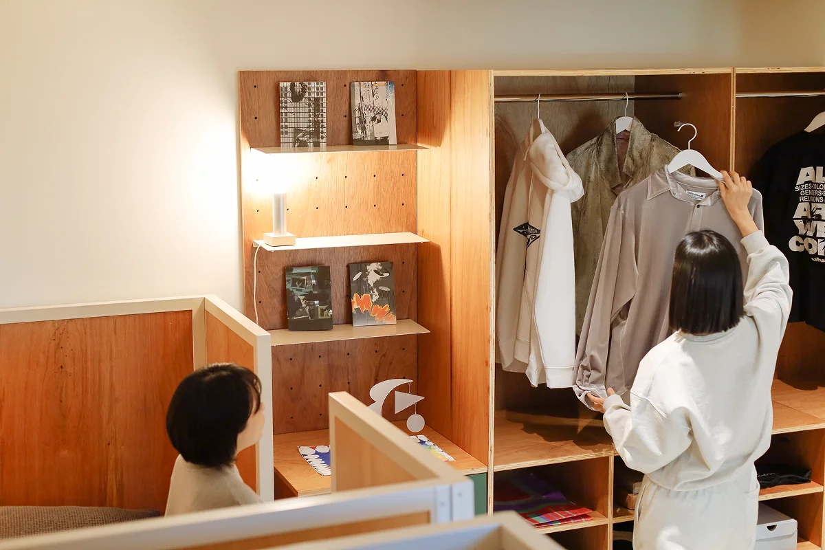 맹그로브 신설 장기 숙박 Twin Deluxe 룸 전경 – 옷장과 수납장이 구비된 객실에서 입주자가 옷을 정리하는 모습. 따뜻한 우드톤 인테리어와 조명으로 장기 체류 고객이 편안하게 생활할 수 있는 코리빙 전용 공간.