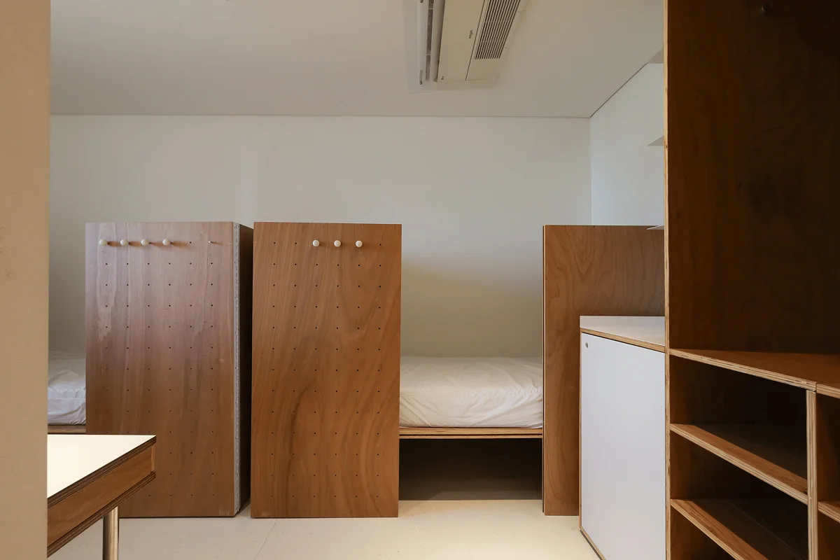 맹그로브 신설 장기 숙박 Twin Deluxe 룸 침실 – 독립된 파티션으로 분리된 침대와 우드톤 인테리어가 특징인 아늑한 객실. 장기 체류 고객이 프라이버시를 유지하며 편안하게 생활할 수 있는 코리빙 숙박 공간.