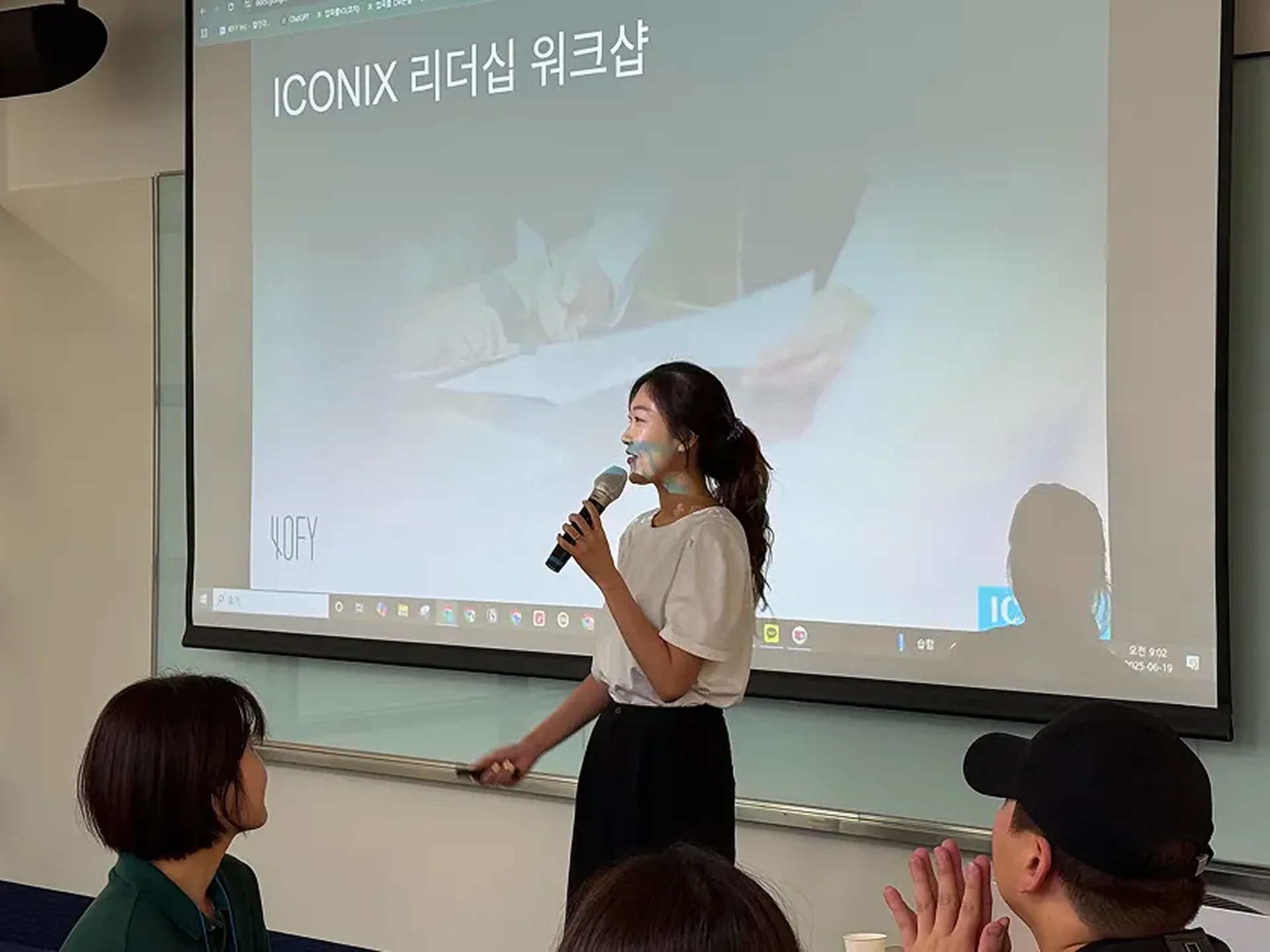 업피플의 황인애 코치님이 스크린 앞에서 마이크를 잡고 청중들에게 워크샵 프로그램에 대해 설명하고 있다.