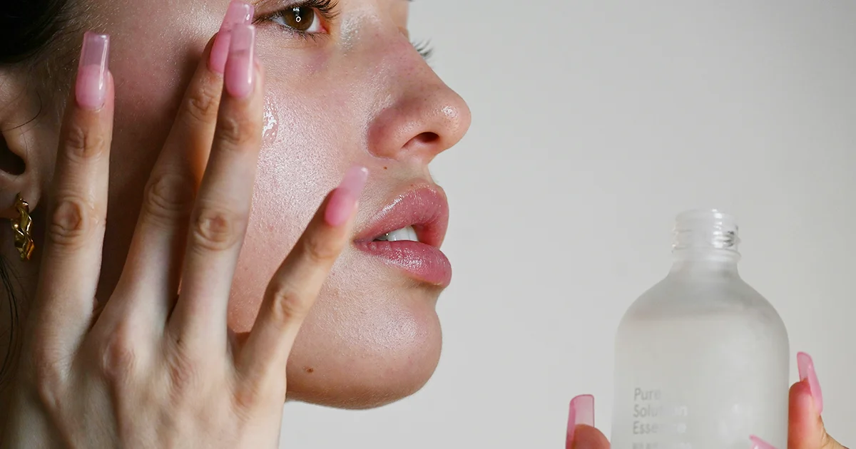 모델이 스킨케어 제품을 손에 들고 얼굴에 에센스를 바르는 클로즈업 컷. 피부 톤과 제품 질감이 강조된 이미지.
