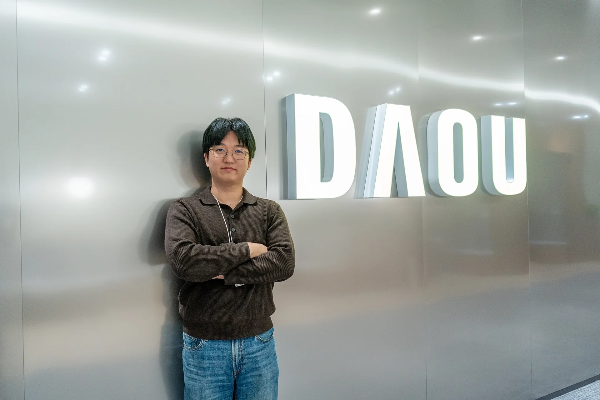 다우오피스HR 마케터 최광래 선임이 DAOU 로고 앞에서 팔짱을 끼고 미소를 짓고 있는 모습