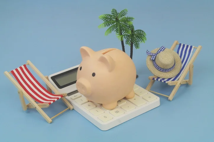 계산기 위에 돼지 저금통이 올려져 있고 그 양옆에는 비치 체어 모형이 놓여있는 모습
